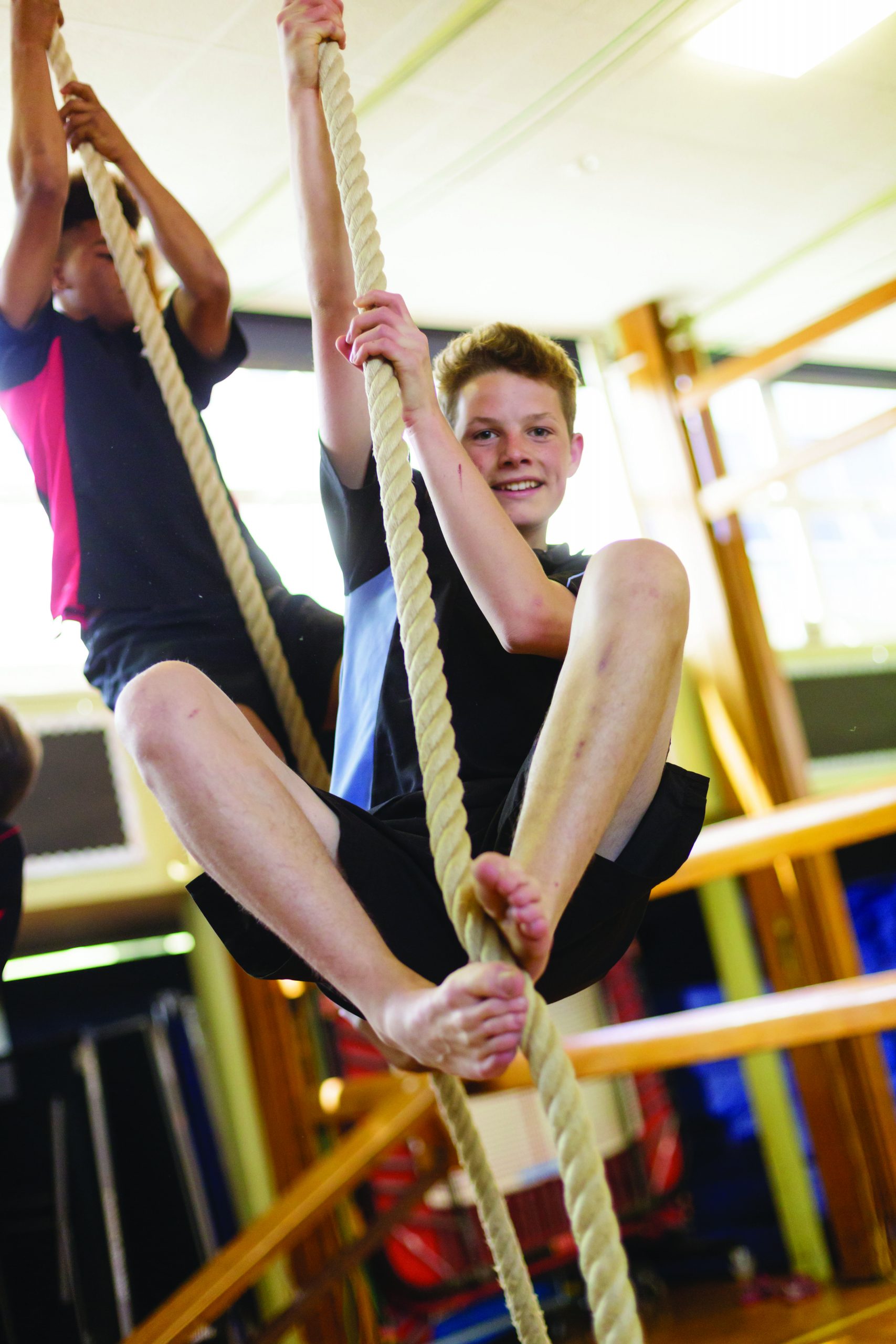 A boy climbing a rope in the gym