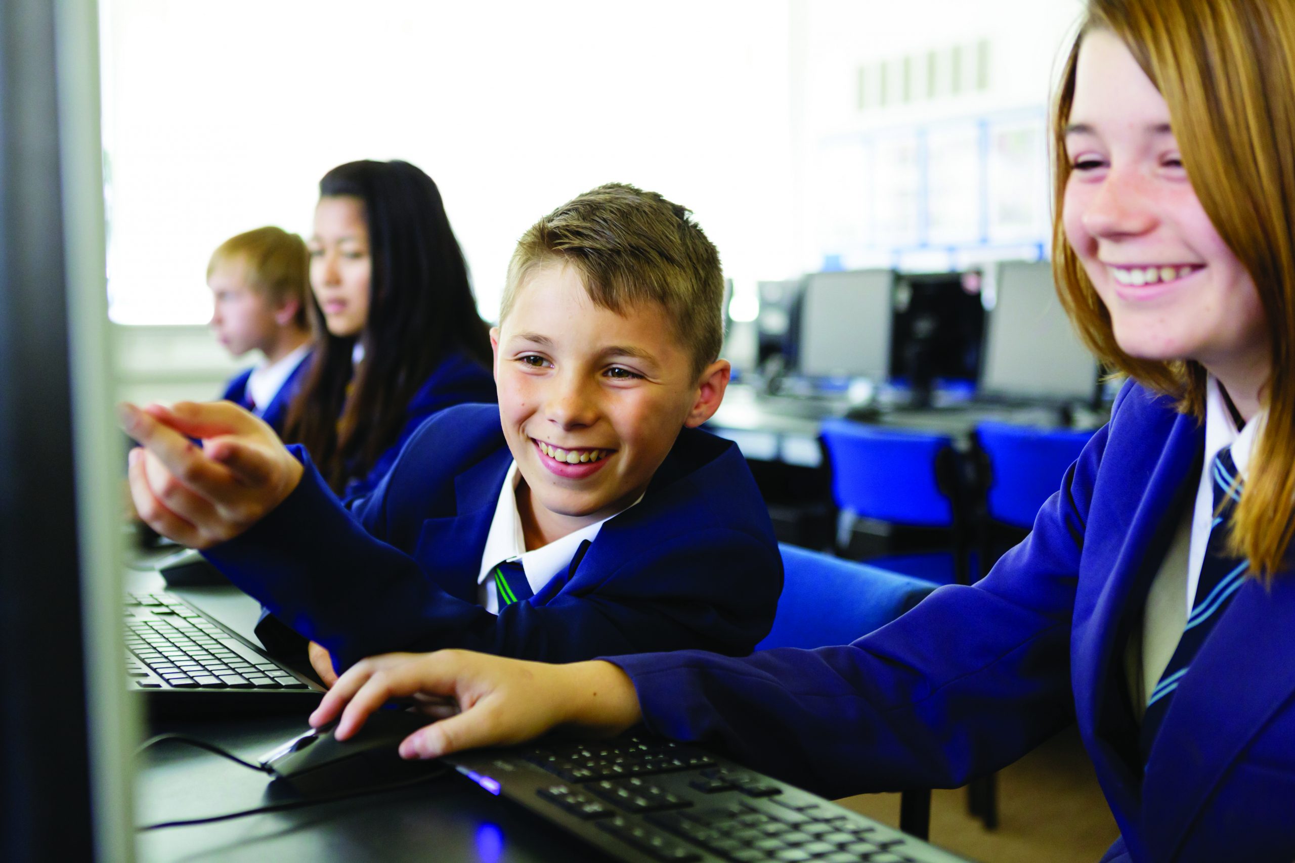 A boy and a girl using a computer. They are smiling and the boy is pointing at the screen