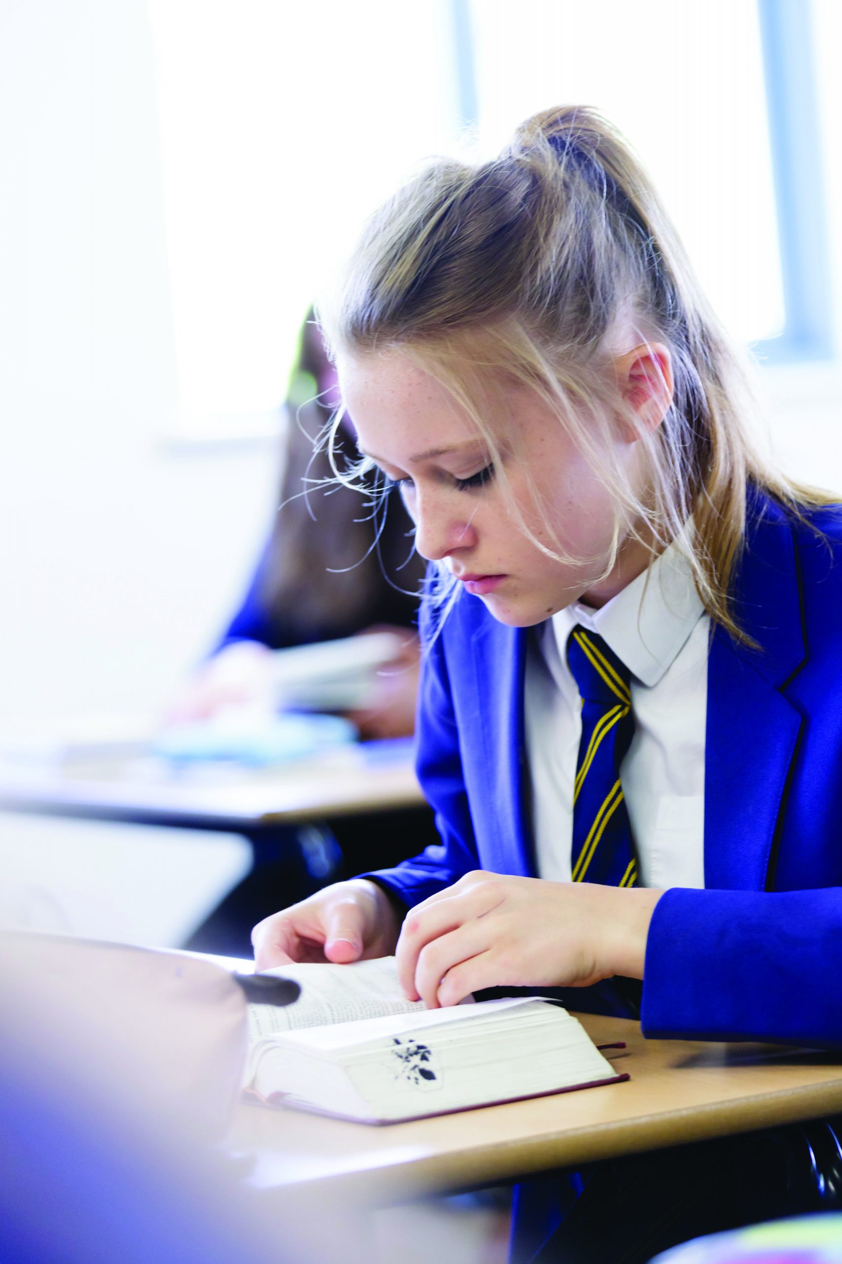 A girl in school uniform sitting at a desk reading a book