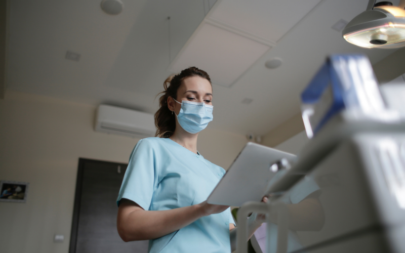 A nurse in a surgical mask looking at a clipboard