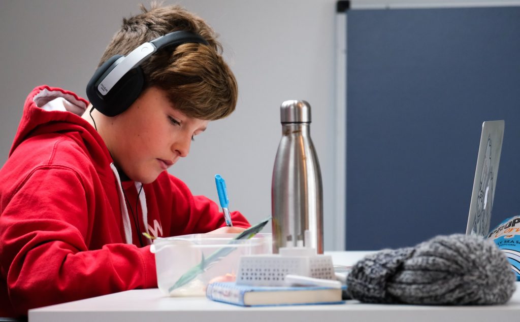 A boy wearing earphones working at a table