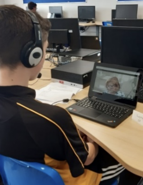A boy wearing a school sports top and headphones, looking at a laptop