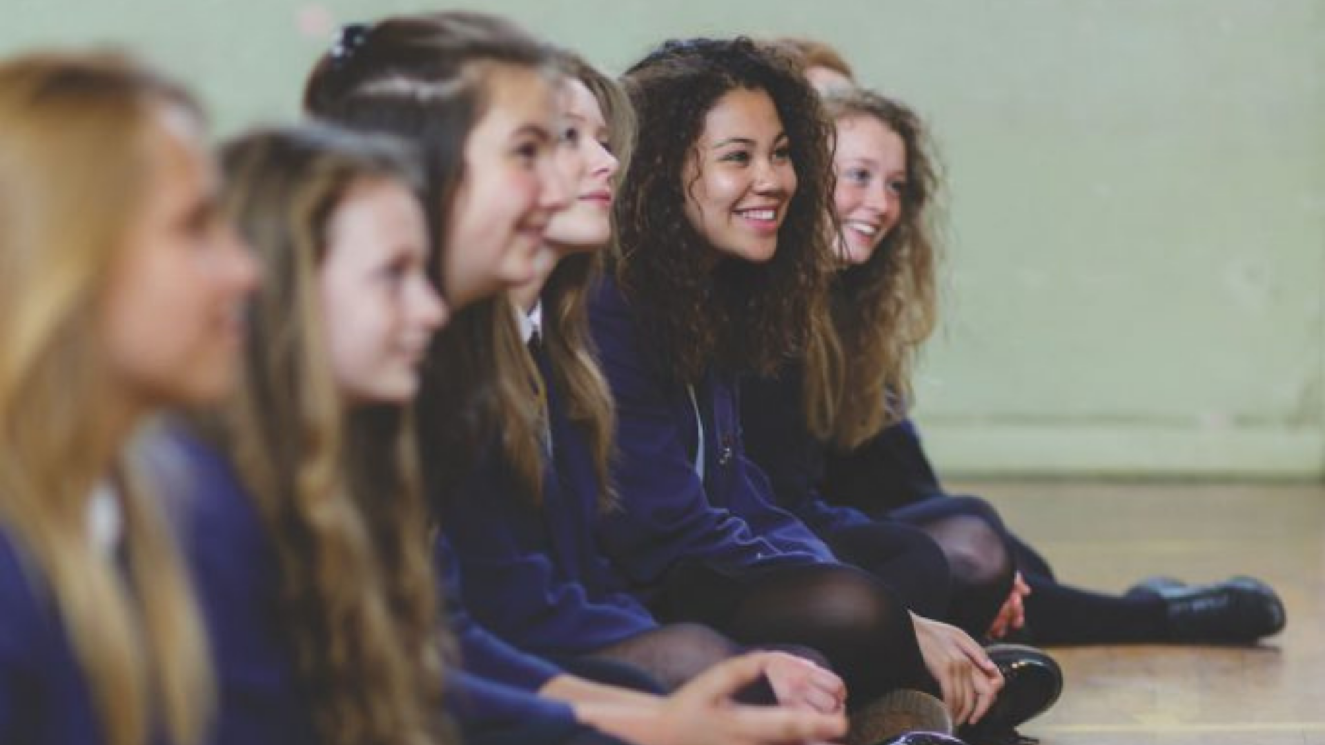 Row of pupils sitting down in the hall, facing forward and smiling