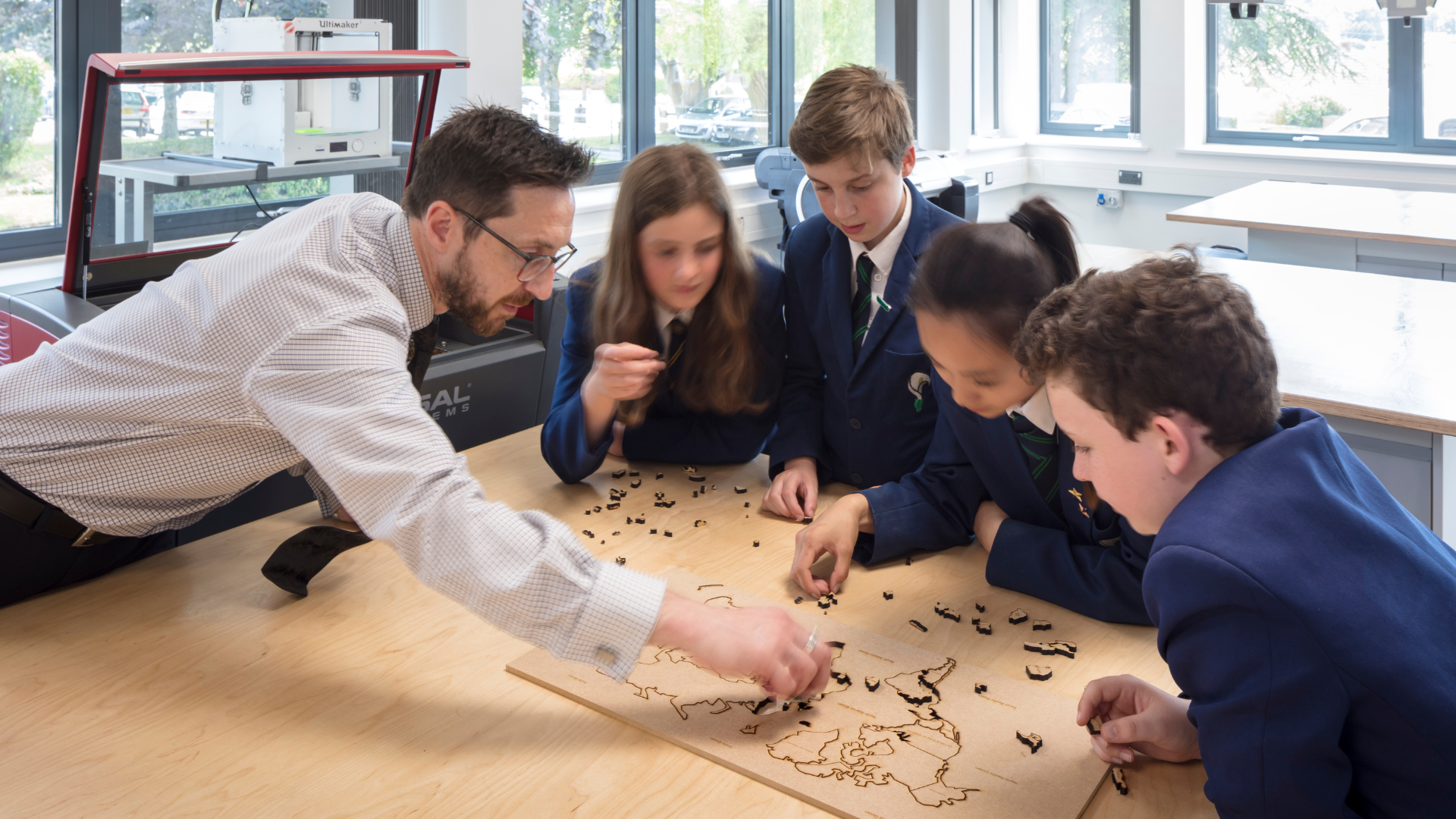 Teacher and 4 pupils standing around a table, working on a project