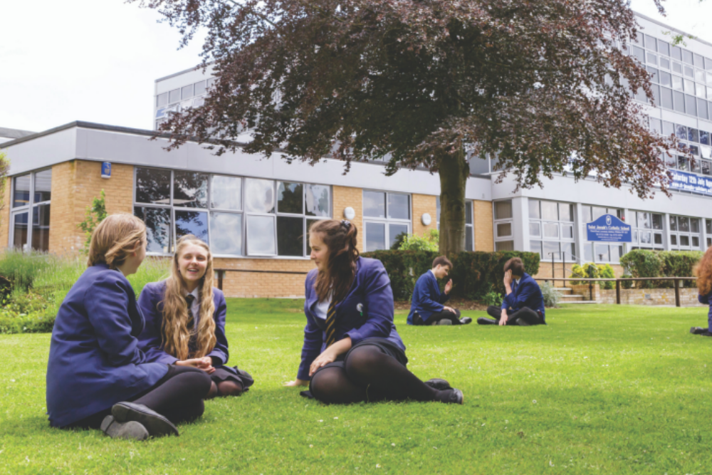 2 separate groups of pupils sit on the grass outside St Joseph's School