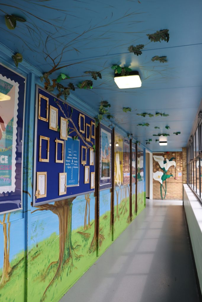 School corridor with posters on the walls, trees painted on the walls and the branches spreading up onto the ceiling, and paper leaves stuck on the branches.